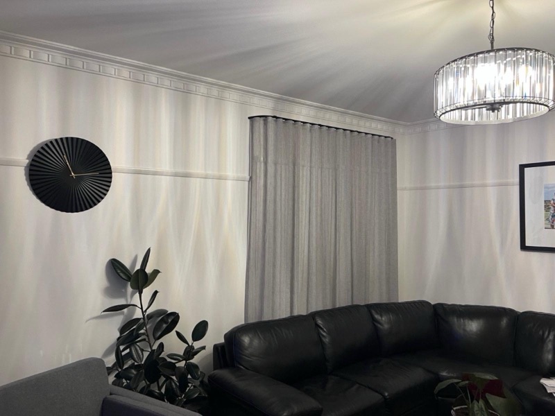 White wave-fold sheers on a black track paired with a white roller blind in an elegant living room with ornate cornice and chandelier