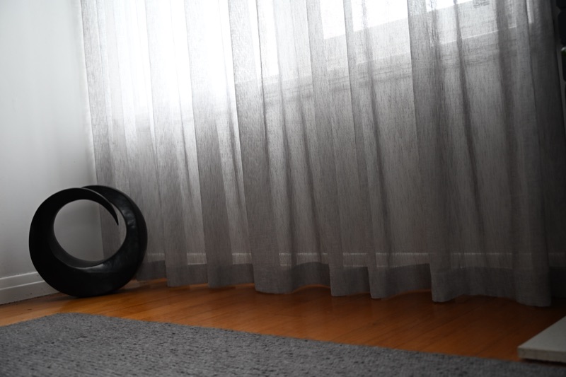 Floor-length grey sheers puddling softly on timber floorboards in a living room, diffusing natural light