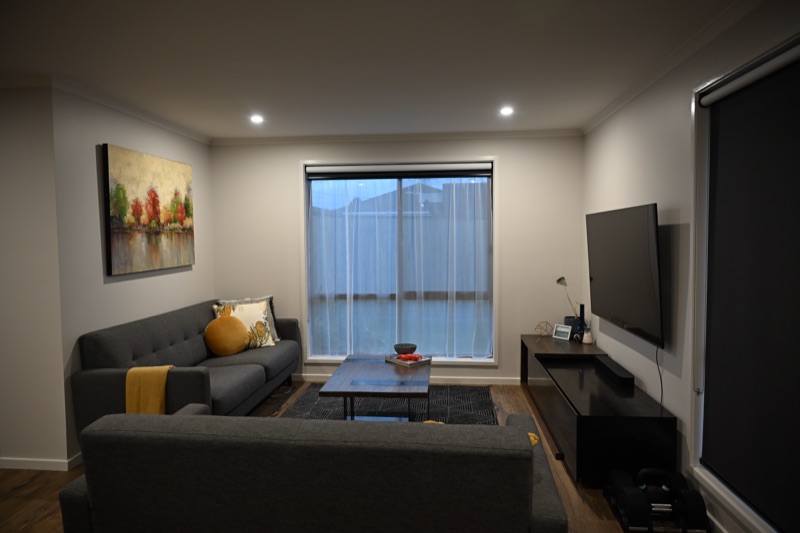 Same living room showing sheer curtains layered with a partially raised charcoal roller blind, both on black tracks