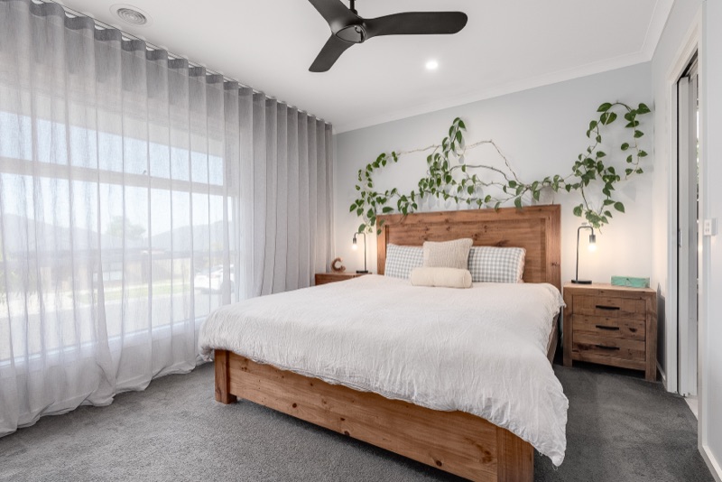 Soft white wave-fold sheers puddling gently at floor level beside a timber bed frame in a bright master bedroom